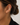 A close-up of a model's ear wearing a polished gold huggie hoop earring, with her hair in a bun and a black top visible against a light background.