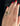 A close-up of a hand with red nail polish wearing a statement ring. The ring features a polished gold heart-shaped centerpiece set on a silver band paved with small clear stones, photographed against a dark background.