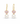 A pair of gold drop earrings featuring a light pink heart-shaped enamel charm with a small clear crystal, and a white pearl dangling below, set against a plain white background.