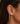A close-up of a model's ear wearing a delicate gold ear cuff with a dangling teardrop chain of clear gemstones.