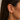 A close-up of a model's ear wearing a delicate gold ear cuff with a dangling teardrop chain of clear gemstones.