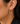 A close-up of a model's ear wearing a gold hoop earring adorned with small clear pavé stones. The earring features a single round clear stone at the top post.
