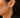 A close-up of a model's ear wearing a gold hoop earring adorned with small clear pavé stones. The earring features a single round clear stone at the top post.