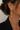 A close-up of a model's ear wearing a gold butterfly drop earring with clear crystal accents, paired with a black blazer against a light neutral background.