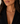 A close-up of a woman wearing a delicate gold necklace with small dark blue and white bead accents, paired with a black blazer.