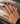 A close-up of a hand with dark burgundy nail polish wearing a wide gold ring with a central pavé band, resting on a beige textured surface.