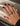 A close-up of a hand with dark burgundy nail polish wearing a wide gold ring with a central pavé band, resting on a beige textured surface.