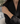 A close-up of a woman wearing a delicate, thin silver chain bracelet on her wrist, paired with a black satin blazer.