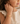 A close-up of a young girl wearing a delicate gold nameplate bracelet with small red bead accents, paired with a cream-colored ruffled dress.