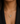 A close-up of a model wearing a gold heart-shaped pendant necklace adorned with colorful gemstones, styled with a black blazer.