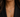A close-up of a model wearing a gold heart-shaped pendant necklace adorned with colorful gemstones, styled with a black blazer.
