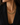 A close-up of a model wearing a gold statement necklace with green rectangular gemstones and small clear stones, styled with a black blazer.