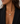 A close-up of a woman wearing a delicate gold chain necklace with an oval pendant featuring a clear, textured stone, styled with a black blazer.