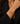 A close-up of a model's wrist wearing a gold chain-link bracelet with a toggle clasp, styled with a black blazer.