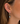 A close-up of a model's ear wearing a gold hoop earring in the cartilage and a matching drop earring with a row of clear stones and a dark gray oval pendant.