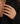 A close-up of a woman's hand wearing a sparkling diamond ring with a silver-toned setting, styled on her ring finger against a black blazer.