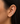 A close-up of a model's ear wearing a small gold huggie hoop earring adorned with clear pavé gemstones.