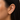 A close-up of a model's ear wearing a small gold huggie hoop earring adorned with clear pavé gemstones.
