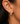 A close-up of a person's ear wearing a pair of gold huggie hoop earrings, one textured and one set with small clear stones.