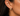 A close-up of a person's ear wearing a pair of gold huggie hoop earrings, one textured and one set with small clear stones.