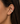 A close-up of a model's ear wearing a delicate gold ear cuff adorned with small clear stones.