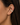 A close-up of a model's ear wearing a delicate gold ear cuff adorned with small clear stones.