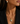 A close-up of a woman wearing a gold chain necklace with a spherical pendant, one side of which is encrusted with small clear stones. She is wearing a black blazer and a matching gold and stone stud earring.