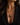 A close-up of a model wearing a gold chain necklace with a dark, irregularly shaped pendant featuring a white letter 'A'. The model is wearing a black blazer.