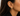 A close-up of a model's ear wearing a small gold huggie hoop earring with a central geometric design.