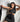 A woman modeling a black satin two-piece set consisting of a halter crop top and a matching high-waisted mini skirt, posing against a white studio background.